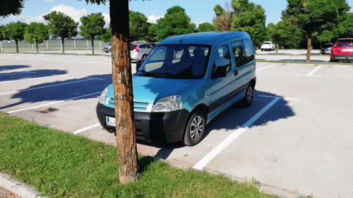 A Blue Van Is Parked In A Parking Lot With A Tree In The Foreground GIF