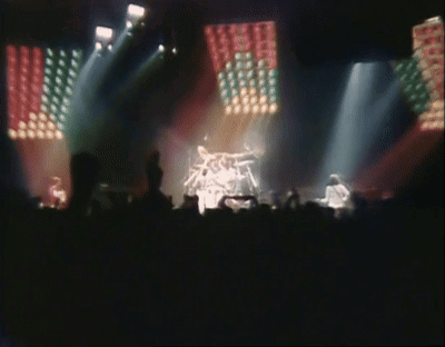 A Blurred Image Of A Band On Stage With A Crowd Watching GIF