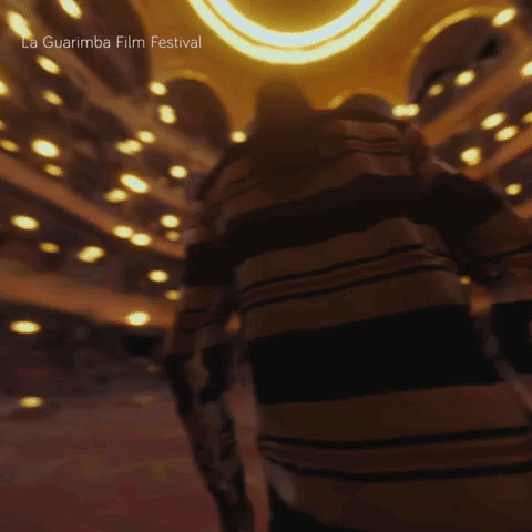 A Blurred Image Of A Person In A Dark Room With The Words La Guarimba Film Festival Visible GIF