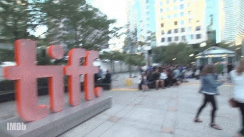 A Blurred Image Of People Walking In Front Of A Large Tiff Sign GIF