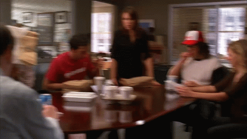 A Blurry Picture Of A Group Of People Sitting Around A Table With A Man Wearing A Red Shirt That Says Supreme GIF