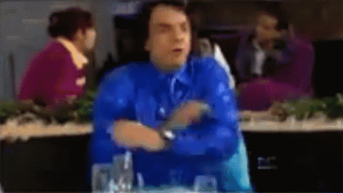 A Blurry Picture Of A Man In A Blue Shirt And Tie Sitting At A Table GIF