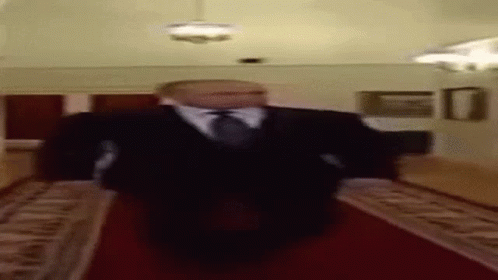 A Blurry Picture Of A Man In A Suit And Tie Walking Down A Red Carpet . GIF