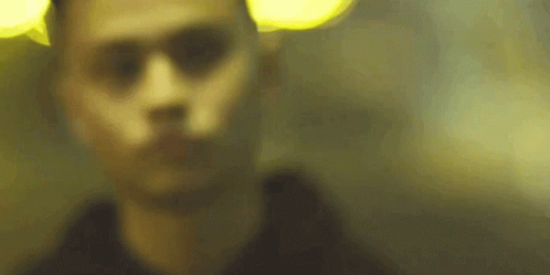 A Blurry Picture Of A Man 'S Face In A Dark Room With A Yellow Light Behind Him . GIF