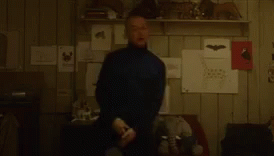 a blurry picture of a man standing in a room with a shelf full of drawings .