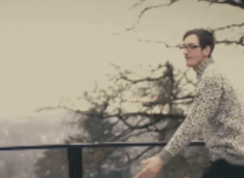 A Blurry Picture Of A Man Standing On A Balcony With A Tree In The Background GIF