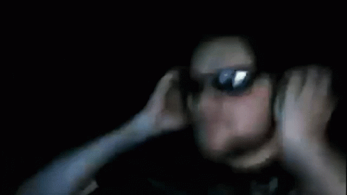 A Blurry Picture Of A Person Covering Their Ears In The Dark GIF