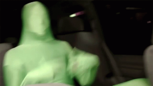 A Blurry Picture Of A Person In A Green Suit Sitting In A Car . GIF