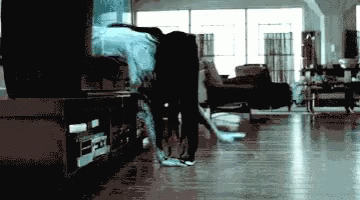 A Blurry Picture Of A Person In A Living Room With A Tv In The Background GIF