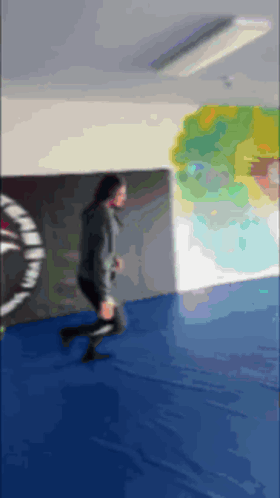 A Blurry Picture Of A Person Running On A Blue Mat In A Gym GIF