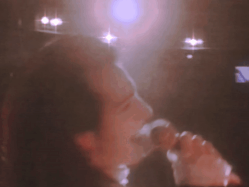 A Blurry Picture Of A Person Singing Into A Microphone . GIF