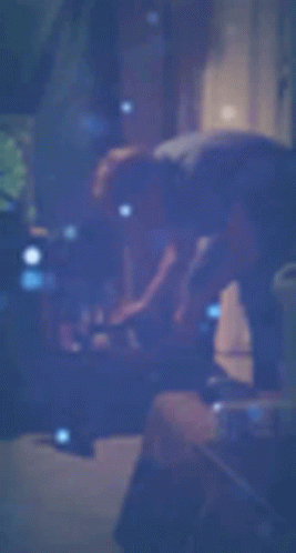 A Blurry Picture Of A Person Standing In A Dark Room With A Blue Background . GIF