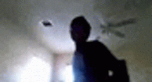 A Blurry Picture Of A Person Standing In A Room With A Ceiling Fan In The Background . GIF