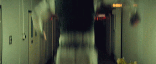 A Blurry Picture Of A Person Walking Down A Hallway With A Sign That Says Emergency Exit GIF
