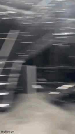 A Blurry Picture Of A Person Walking Down Stairs In A Dark Room . GIF