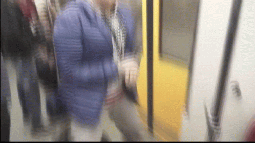 A Blurry Picture Of A Woman In A Blue Jacket Walking On A Train GIF
