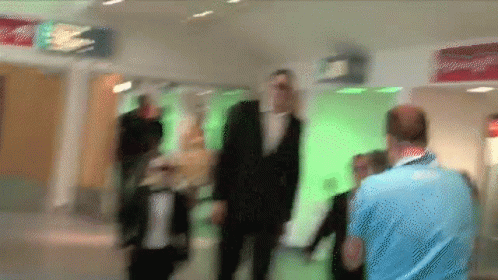 A Blurry Picture Of People Walking In A Hallway With A Red Sign That Says Exit GIF