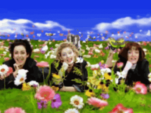 A Blurry Picture Of Three Women Laying In A Field Of Flowers GIF