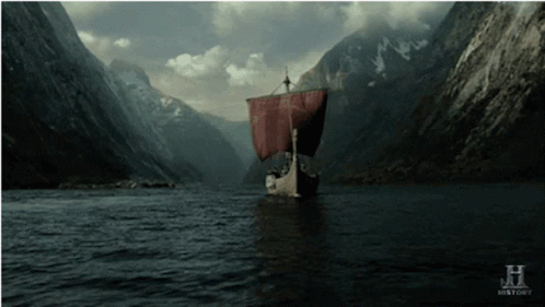 A Boat With A Red Sail Is Floating In A River With Mountains In The Background GIF