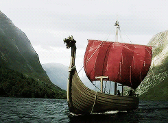 A Boat With A Red Sail Is Floating On A Body Of Water GIF