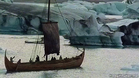 A Boat With A Sail Is In The Water With Icebergs In The Background GIF