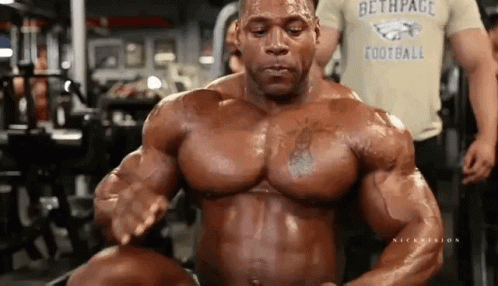 A Bodybuilder Is Flexing His Muscles In A Gym While Wearing A Football Shirt . GIF