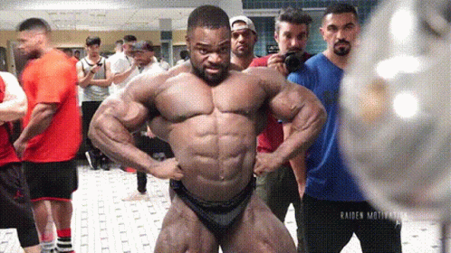 A Bodybuilder Is Posing For A Picture In Front Of A Group Of People . GIF