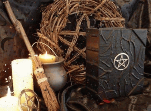 A Book With A Pentagram On It Sits On A Table Next To Candles And A Broom GIF