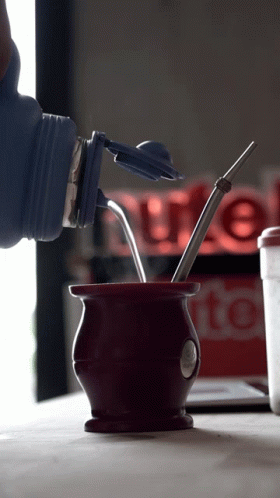 A Bottle Is Being Poured Into A Cup With A Straw In It GIF