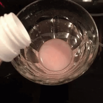 A Bottle Is Being Poured Into A Glass Of Liquid GIF