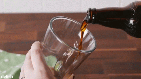 A Bottle Of Beer Is Being Poured Into A Glass By A Person GIF