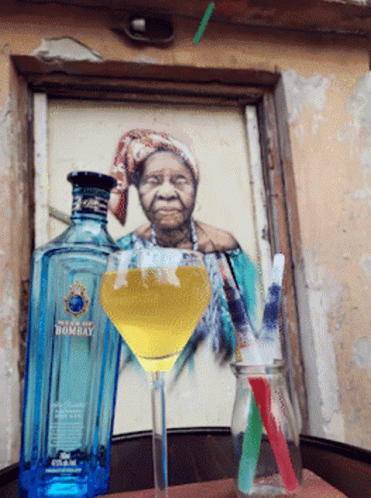 A Bottle Of Bombay Sits Next To A Martini Glass With A Straw GIF