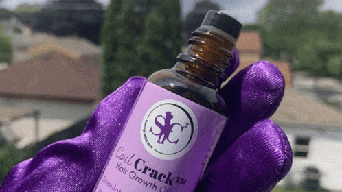 A Bottle Of Coil Crack Hair Growth Oil Is Being Held In A Purple Glove GIF