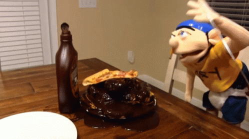 A Bottle Of Ketchup Sits On A Table Next To A Puppet With The Letter Y On His Shirt GIF