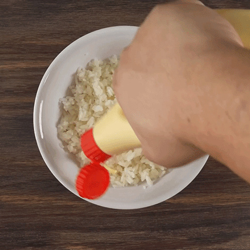 A Bottle Of Mayonnaise Is Being Poured Over Rice On A Plate GIF