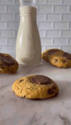A Bottle Of Milk Sits Next To Three Cookies GIF