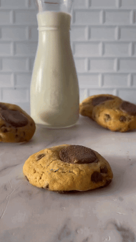 A Bottle Of Milk Sits Next To Three Cookies GIF