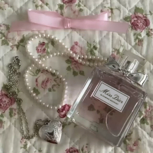 A Bottle Of Miss Dior Perfume Sits On A Bed Next To A Pearl Necklace GIF
