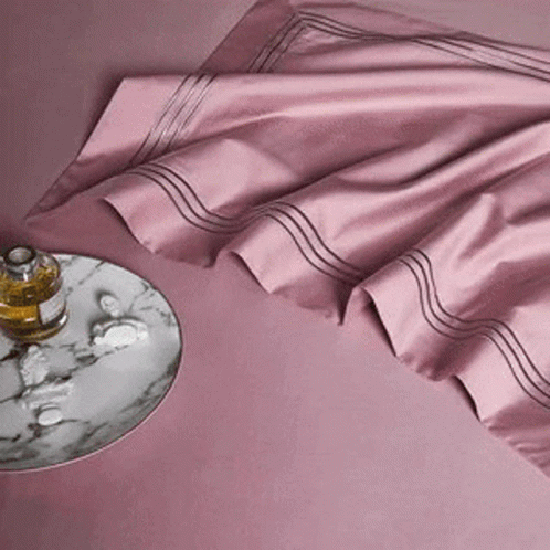 A Bottle Of Perfume Sits On A Marble Tray Next To A Pink Sheet . GIF