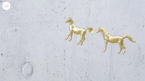 A Bottle Of Woodford Reserve Whiskey Next To A Pair Of Gold Horse Earrings GIF