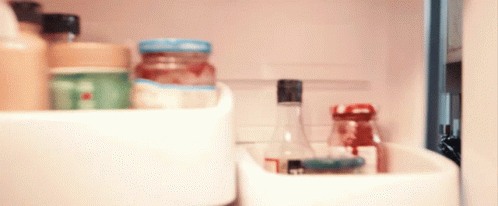 A Bottle With A Black Cap Sits In A Refrigerator Shelf GIF