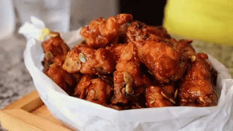 A Bowl Of Fried Chicken Wings Is Wrapped In Wax Paper GIF