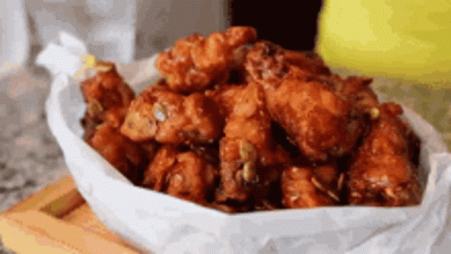 A Bowl Of Fried Chicken Wings Wrapped In Wax Paper On A Wooden Cutting Board . GIF