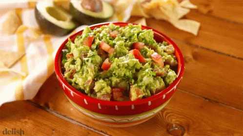 A Bowl Of Guacamole Sits On A Wooden Table Next To A Pile Of Tortilla Chips GIF