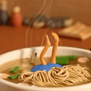 A Bowl Of Noodles With A Person 'S Legs Sticking Out Of It On A Table . GIF