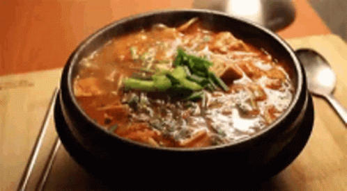 a bowl of soup is sitting on a wooden table next to chopsticks and a spoon .