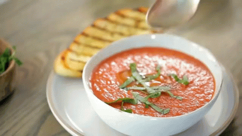 A Bowl Of Tomato Soup Is Being Poured With A Spoon . GIF