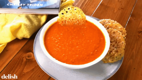 A Bowl Of Tomato Soup Next To A Book By Chrissy Trigon GIF