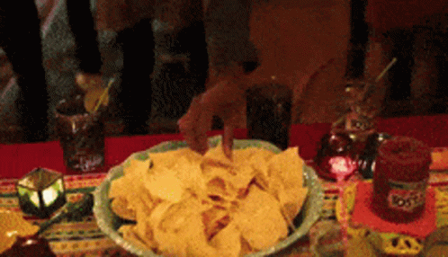 A Bowl Of Tortilla Chips Sits On A Table Next To A Bottle Of Tequila GIF