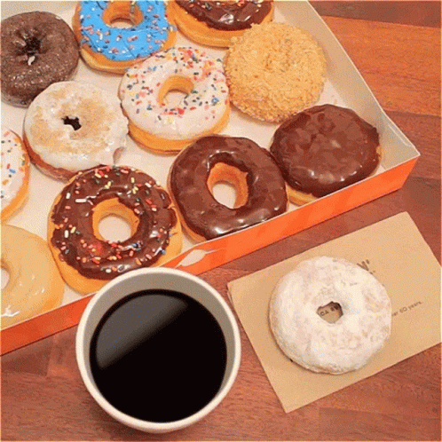 A Box Of Donuts Sits Next To A Cup Of Coffee On A Table GIF